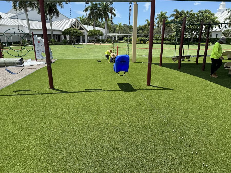 Crew installing artificial turf under a playground swing set