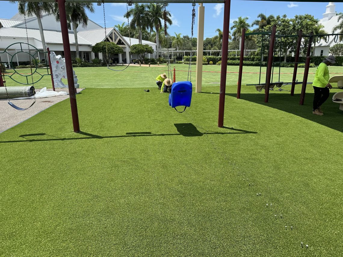Crew installing artificial turf under a playground swing set