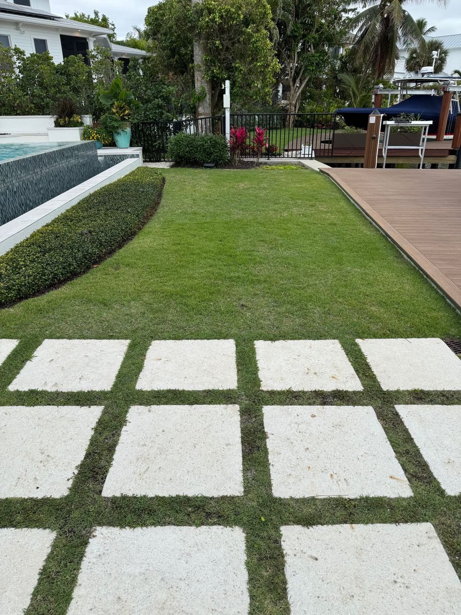 Live grass between stone pavers leading to a waterfront lawn
