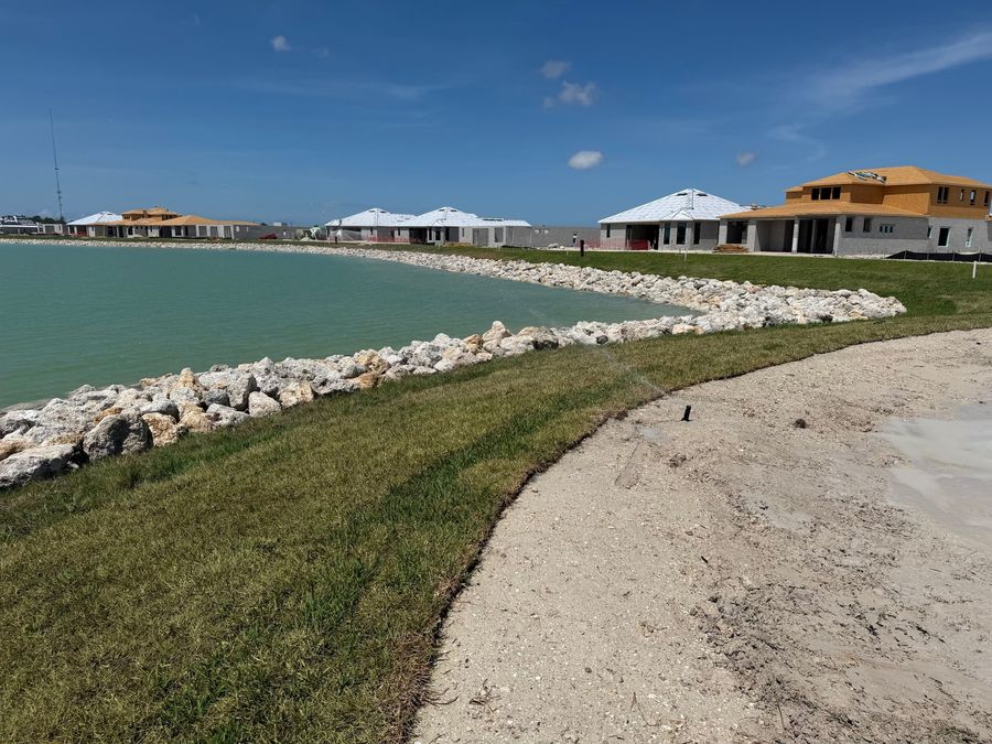 Fresh sod along a riprap lake bank with homes under construction